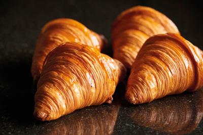Artisan puff pastry croissants with a golden finish and perfect lamination, crafted by master bakers and presented on a dark surface to highlight their texture and quality.