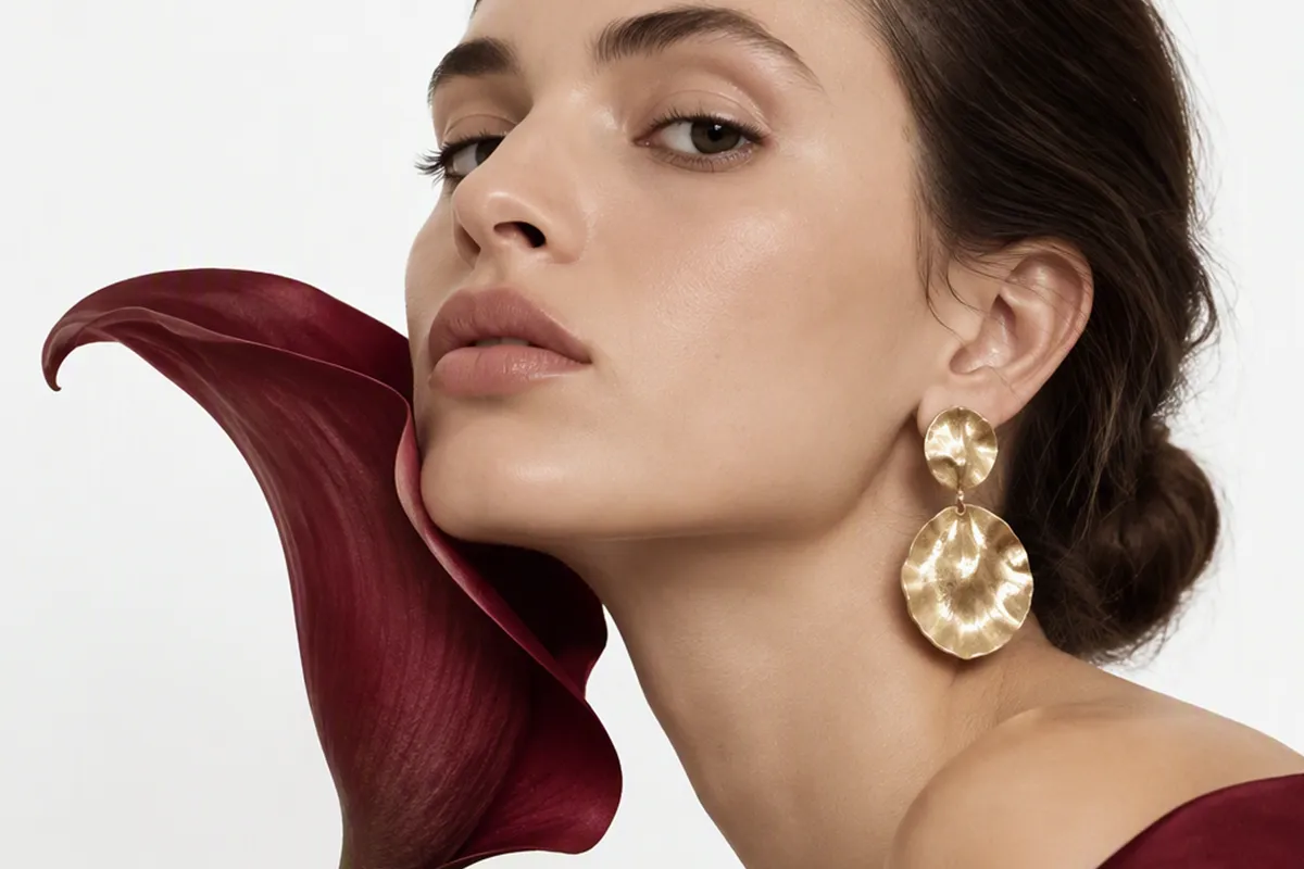 Mujer con pendientes de diseño acariciando a una flor granate