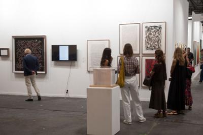 Visitantes observan obras de arte contemporáneo en un stand de feria, con cuadros abstractos y una vitrina expositiva.
