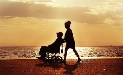 Puesta de sol en playa, señora paseando a una persona en silla de ruedas