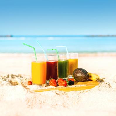  Cuatro vasos con coctails variados y frutas típicas de Canarias sobre un fondo de playa                                                                                                     Cuatro vasos con coctails variados y frutas típicas de Canarias sobre un fondo de playa 