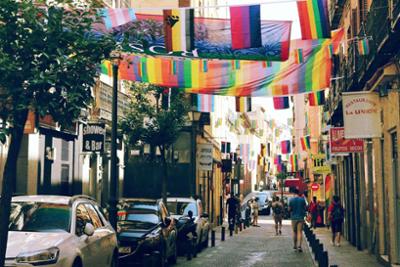 Image of a street with multicolored lgtbt flags hanging from facade to facade.