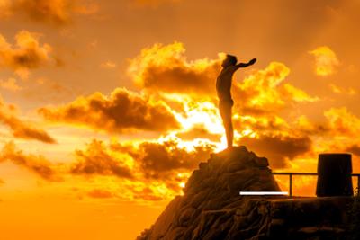 Persona encima de una montaña con los brazos en cruz en un amanecer con el sol detrás Fitur 2026