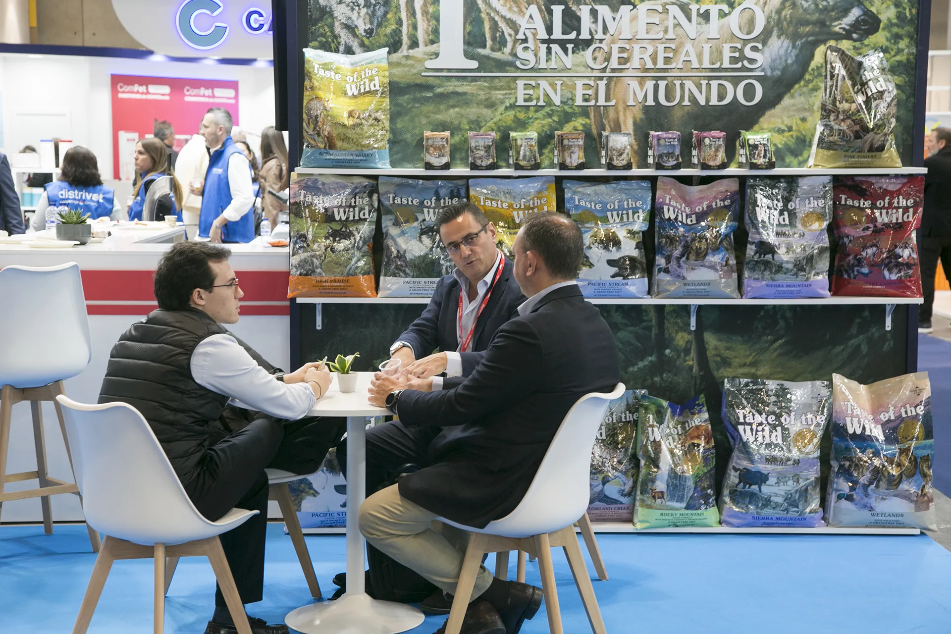 People talking at a stand and behind them shelves of dog food.