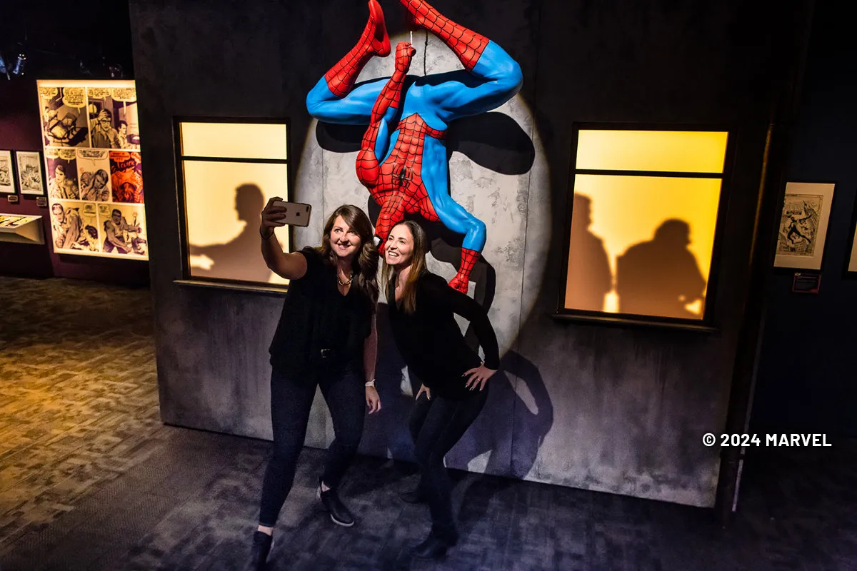 Two girls having their picture taken with a spider-man figure at the Marvel: Universe of Super Heroes exhibition.