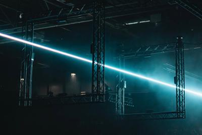 Estructuras metálicas cuadradas suspendidas en un espacio oscuro, atravesadas por un rayo de luz láser azul que crea un efecto futurista e iluminado en medio de la penumbra en un concierto de Outworld