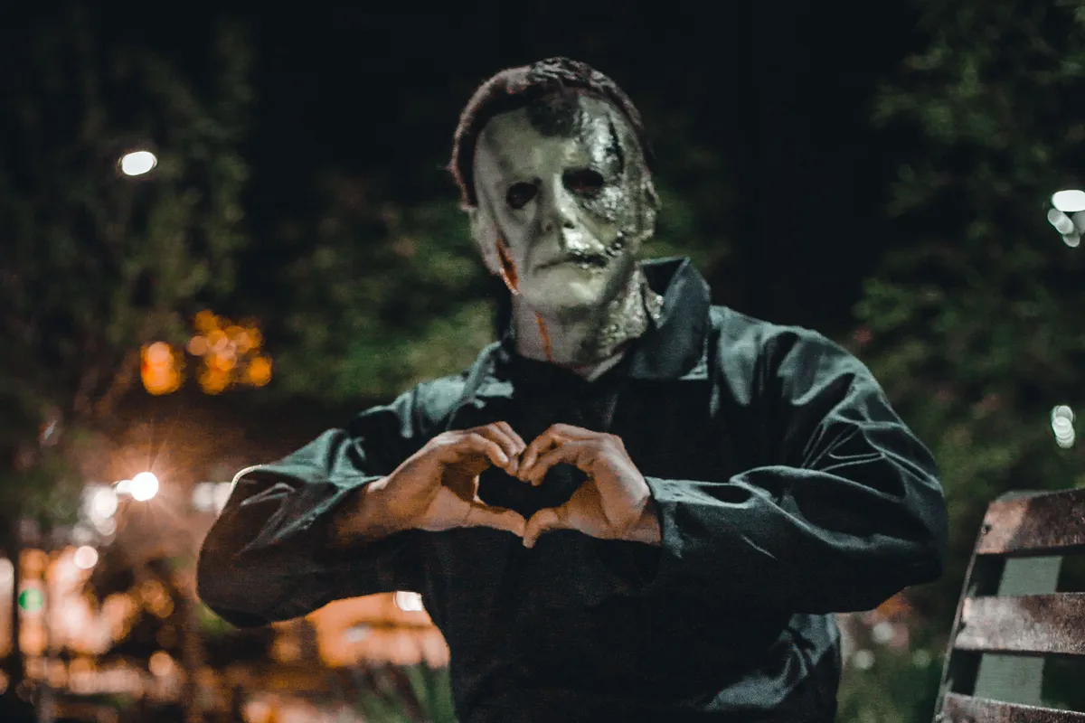 Persona disfrazada de Frankenstein haciendo un corazón sentadoi en un banco por la noche