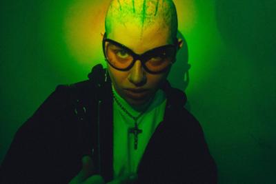 Persona posando en Antídoto Festival con el pelo rapado y con gafas con fondo verde