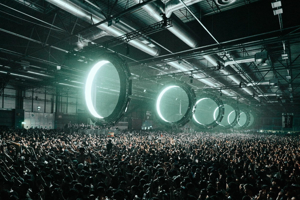 Estructuras metálicas circulares suspendidas en un espacio oscuro, atravesadas por un rayo de luz láser azul que crea un efecto futurista e iluminado en medio de la penumbra en un concierto de Outworld