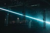 Estructuras metálicas cuadradas suspendidas en un espacio oscuro, atravesadas por un rayo de luz láser azul que crea un efecto futurista e iluminado en medio de la penumbra en un concierto de Outworld