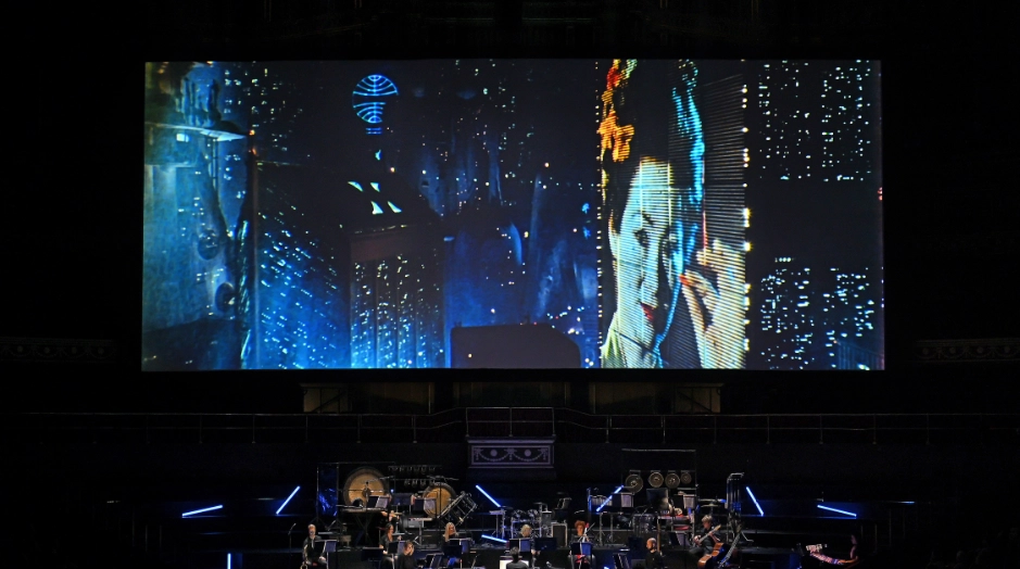 orquesta encima del escenario tocando musica de Blade Runner Live con escena de la película