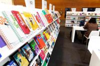 Bookshelf full of books and a table at the back with two people.