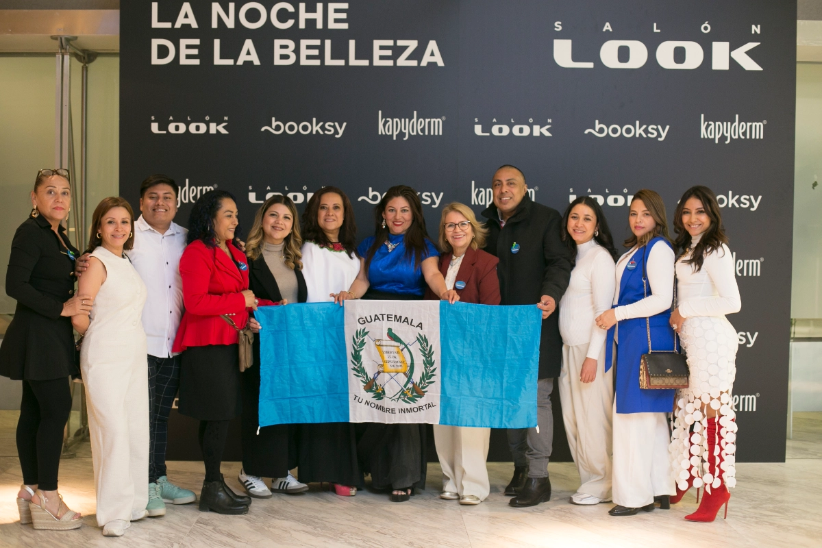 Asistentes a la noche de la belleza en LOOK posando en un photocall con una bandera de guatemala