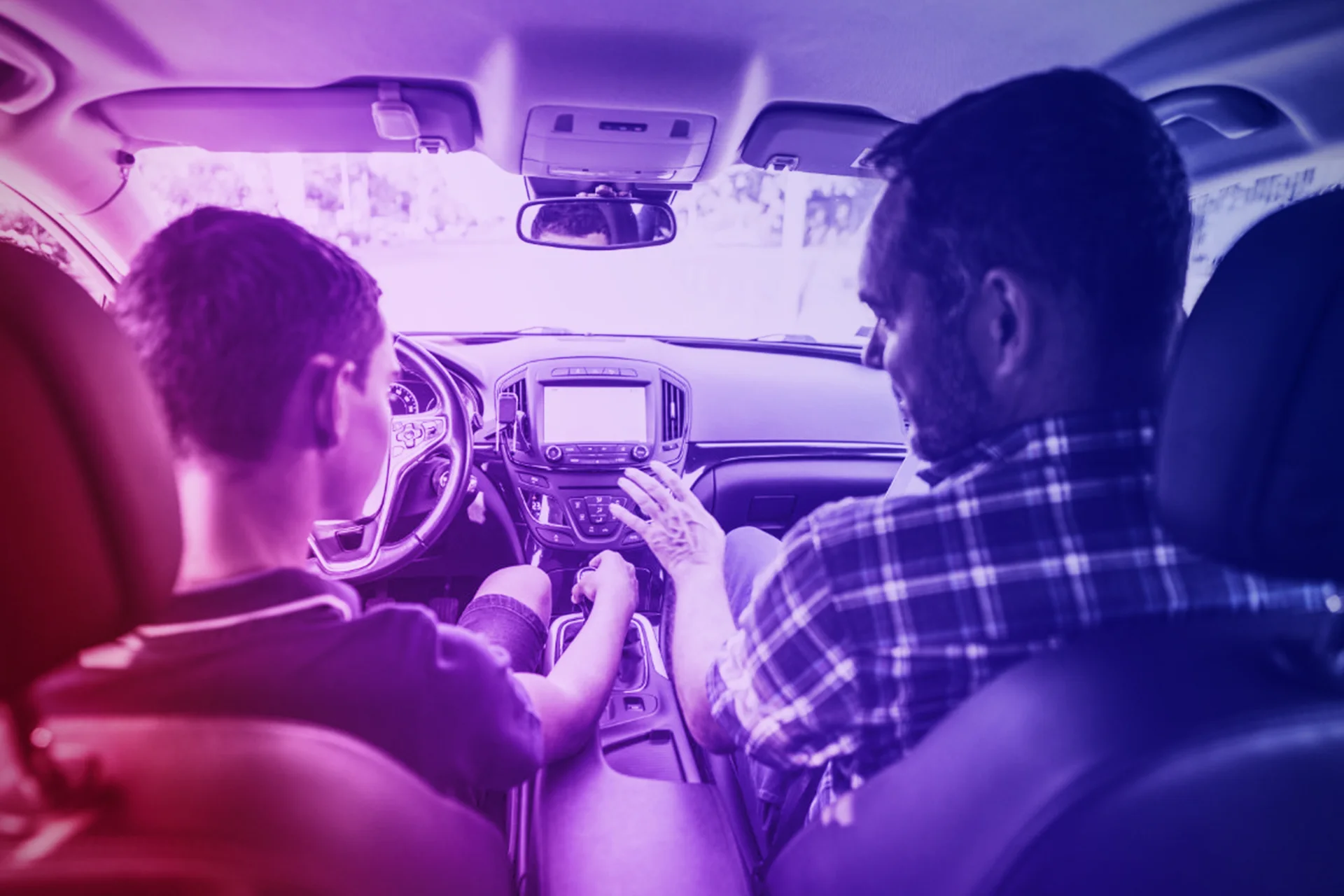 Una mano sujetando un volante y otra navegando en el ordenador central del coche.