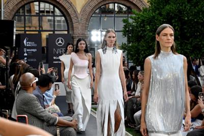 Desfile de Isabel Sanchis en Mercedes-Benz Fashion Week Madrid, con modelos luciendo diseños de alta costura en tonos blancos y plateados sobre una pasarela rodeada de público.