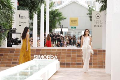Desfile de SIMORRA en Mercedes-Benz Fashion Week Madrid, con modelos presentando diseños de moda contemporánea en una pasarela al aire libre entre vegetación y elementos arquitectónicos.