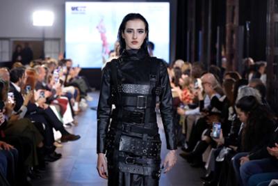 Look total negro con correas y detalles metálicos durante un desfile de moda, ante un público situado a ambos lados de la pasarela.
