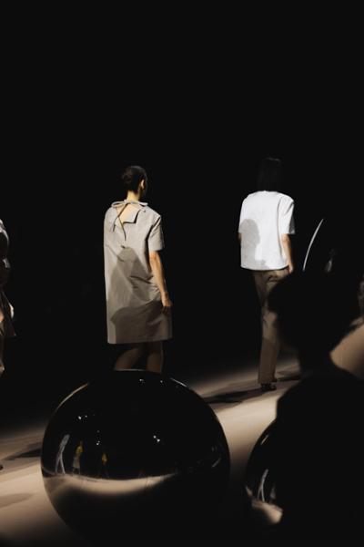 Modelos desfilando en una pasarela de moda con diseño minimalista y esferas reflectantes en primer plano