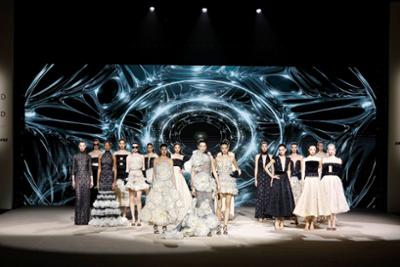 Modelos presentan la colección de Hannibal Laguna sobre la pasarela de Mercedes-Benz Fashion Week Madrid, con vestidos de alta costura en tonos blanco y negro y un espectacular fondo digital futurista.