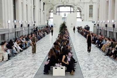 Pasarela de moda en un gran edificio histórico, con público a ambos lados y varias personas desfilando bajo iluminación profesional