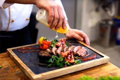 Chef aliñando con aceite unas carnes