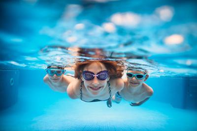 Chica y dos niños buceando en una piscina.