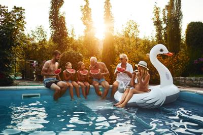 Una familia reunida en el bordillo de una piscina comiendo sandía.