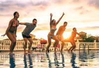 Grupo de amigos y amigas saltando a una piscina en el atardecer.