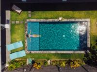 Vista aerea de un jardín con piscina y una chica en ella.