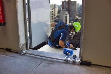 Un operario, a punto de descolgarse de un edificio con un dispositivo de anclaje para jambas