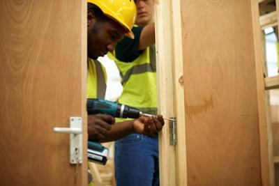 Instalación de una puerta de madera con taladro eléctrico en una estructura en construcción.
