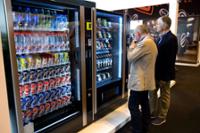 Visitors observing vending machines for soft drinks and snacks.