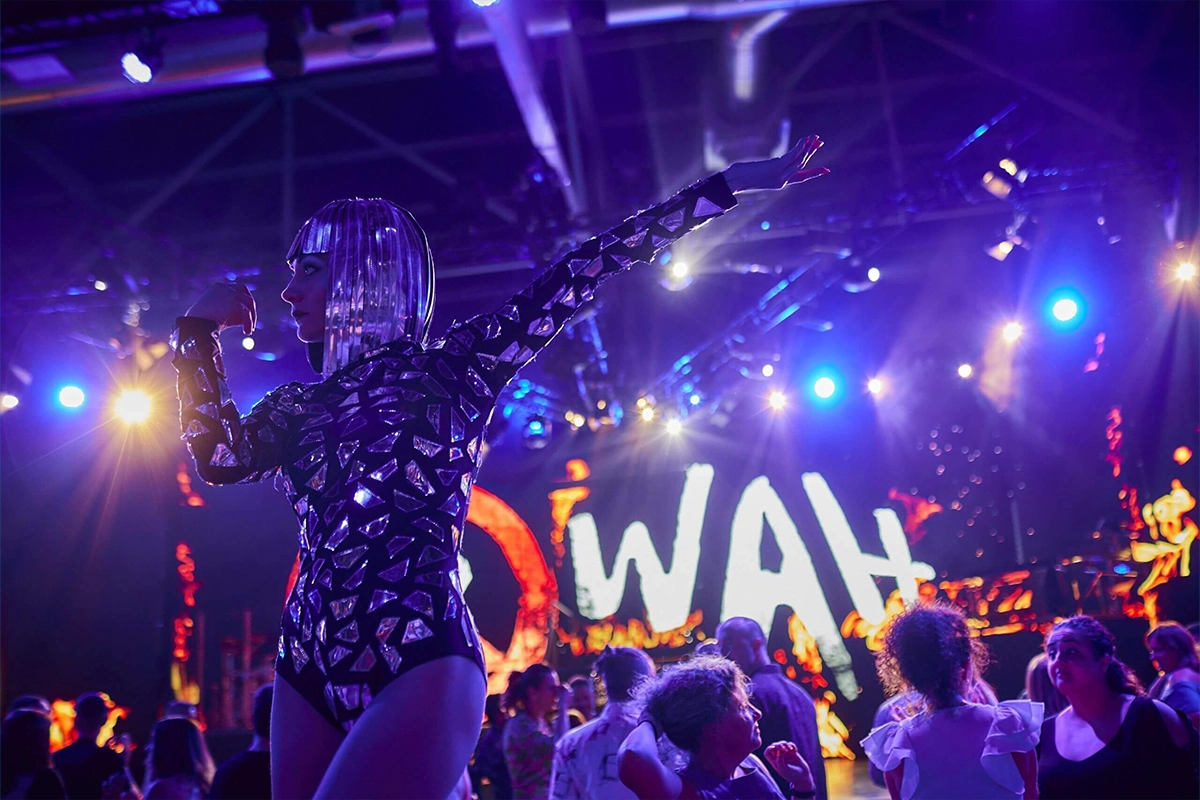 chica con traje de cristales bailando delanta del logo de WAH