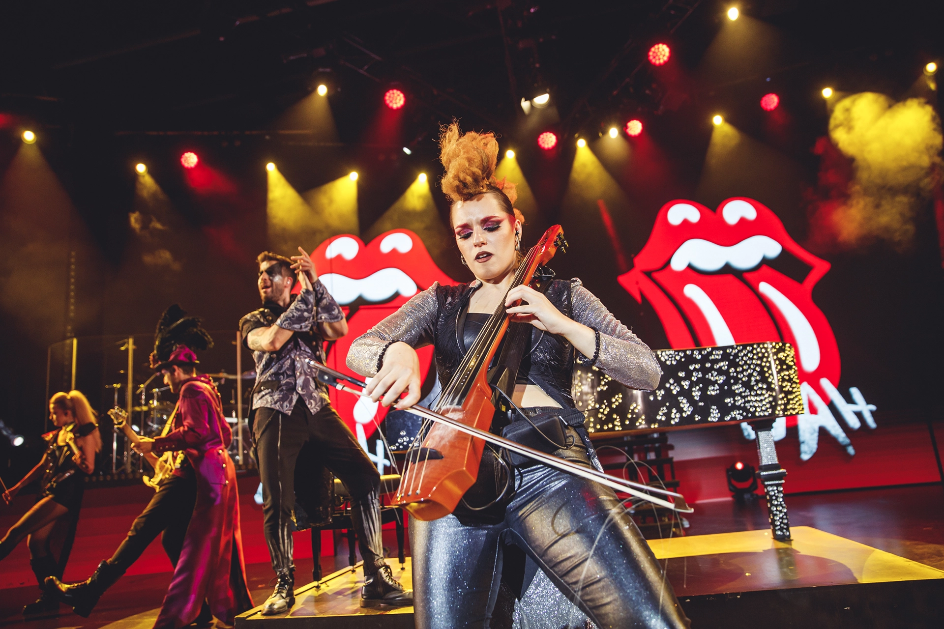 WAH artist playing violin on stage with rolling stones background.